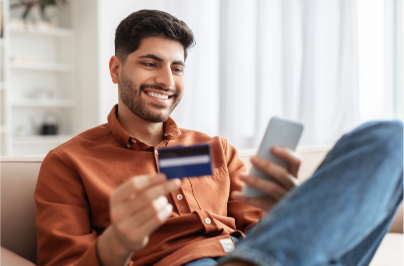 Les meilleures cartes de crédit pour les nouveaux arrivants au Canada - Meilleure CC pour les nouveaux arrivants homme assis avec carte de crédit et téléphone
