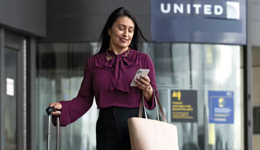 United Premier Access: What Is It and Is It Worth It? - woman on phone with United Airlines signage on back ground